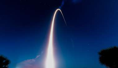 An arcing plume of fire from a rocket launch streaks into the nighttime sky.