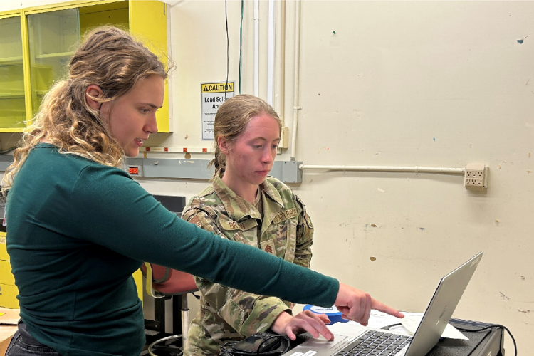 Two women, one cadet and another plain clothed pointing at a computer screen.